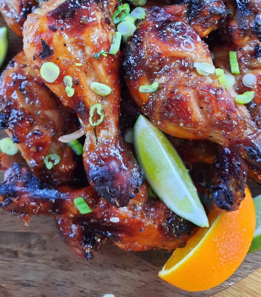 close up of a pile of chicken drumsticks slathered in sauce and segments of orange and lime