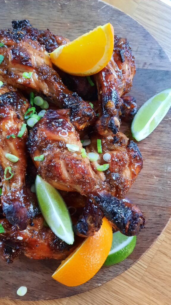 a pile of sticky and sweet chicken drumsticks on a platter sprinkled with green onions