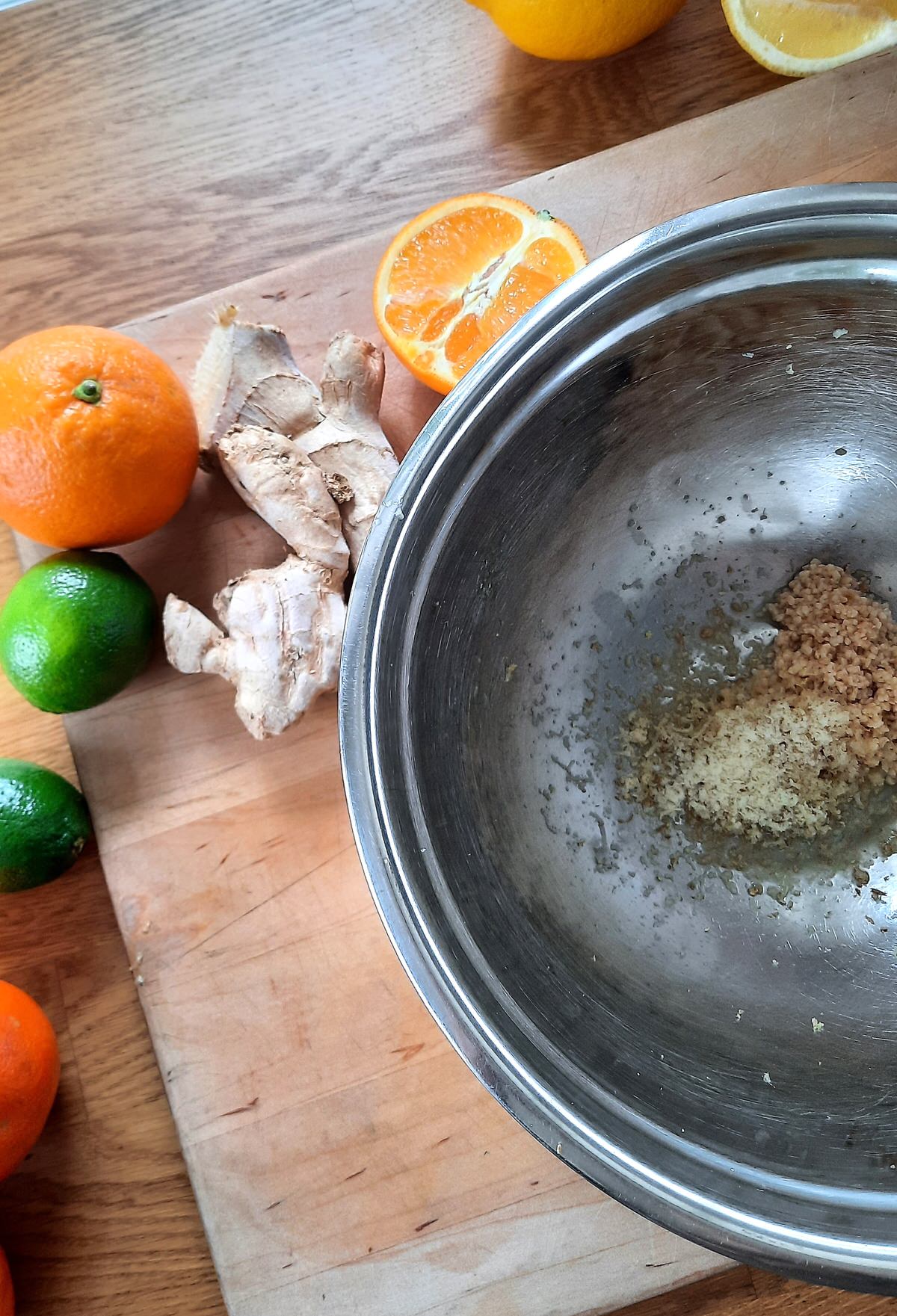 a bowl with chopped ginger and garlic in it sits on a counter beside whole ginger, limes, and oranges