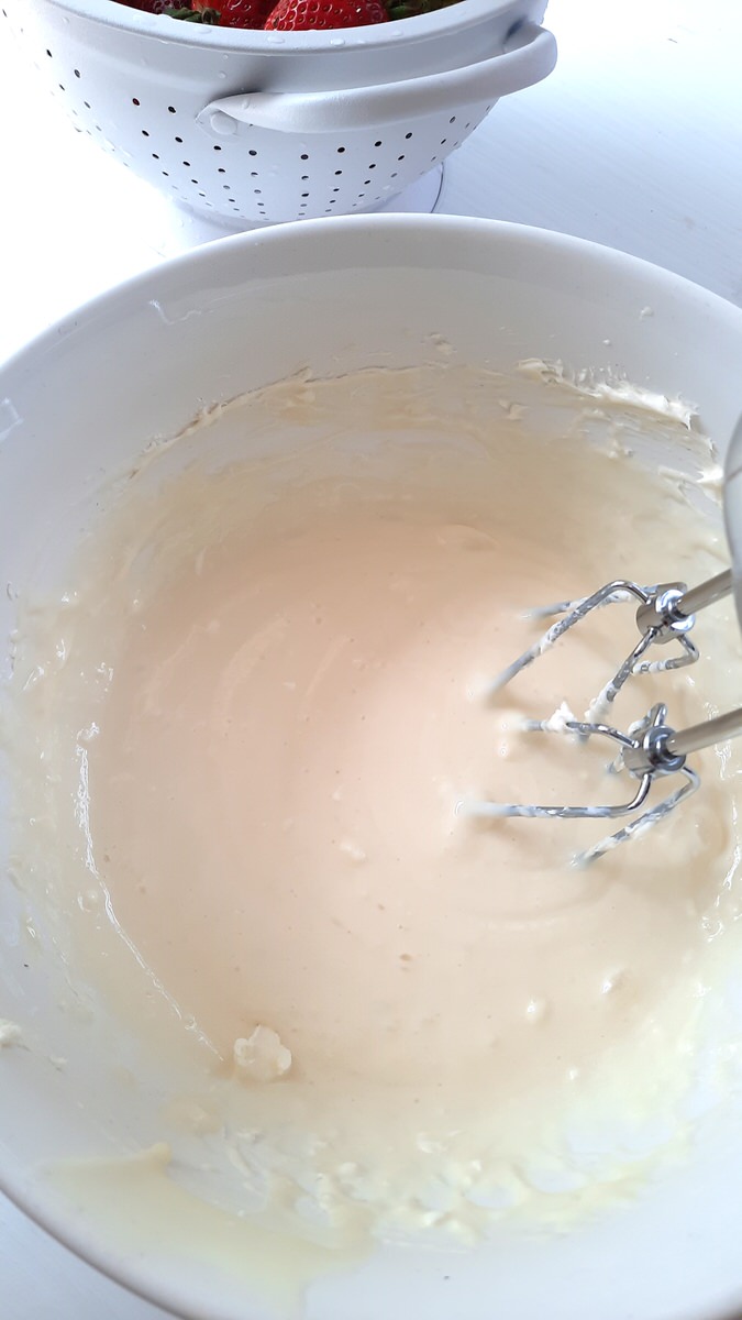 beaters mixing condensed milk and cream cheese in a white bowl