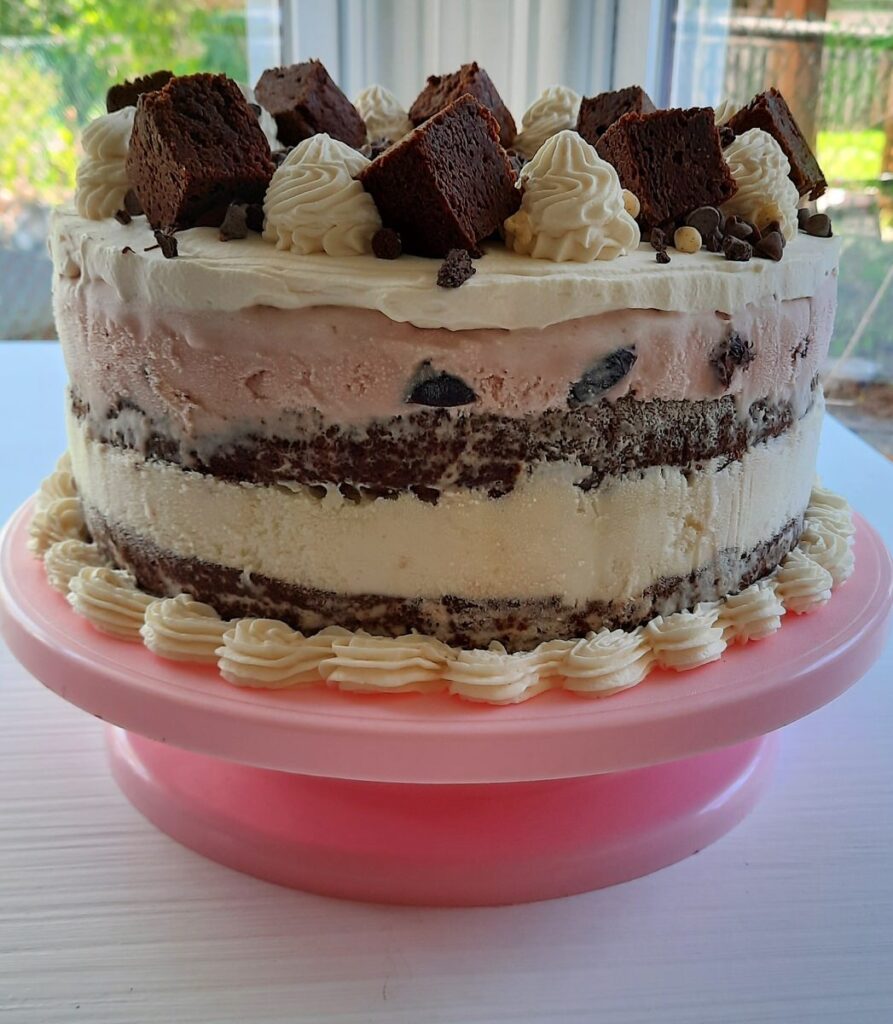 side shot of brownie ice cream cake with layers of brownie and ice cream on a pink cake tray