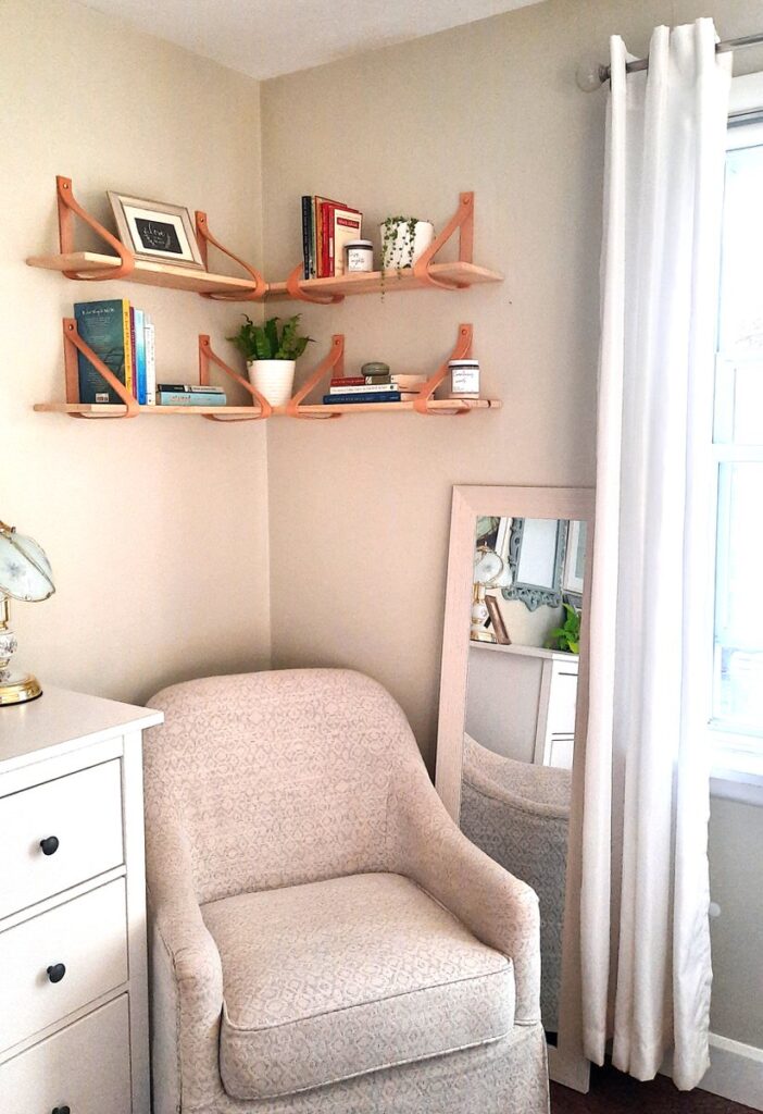 corner of bedroom with corner shelves installed above a white upholstered chair