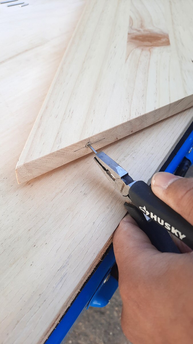 Pressing finishing nails in to board using pliers to hold them