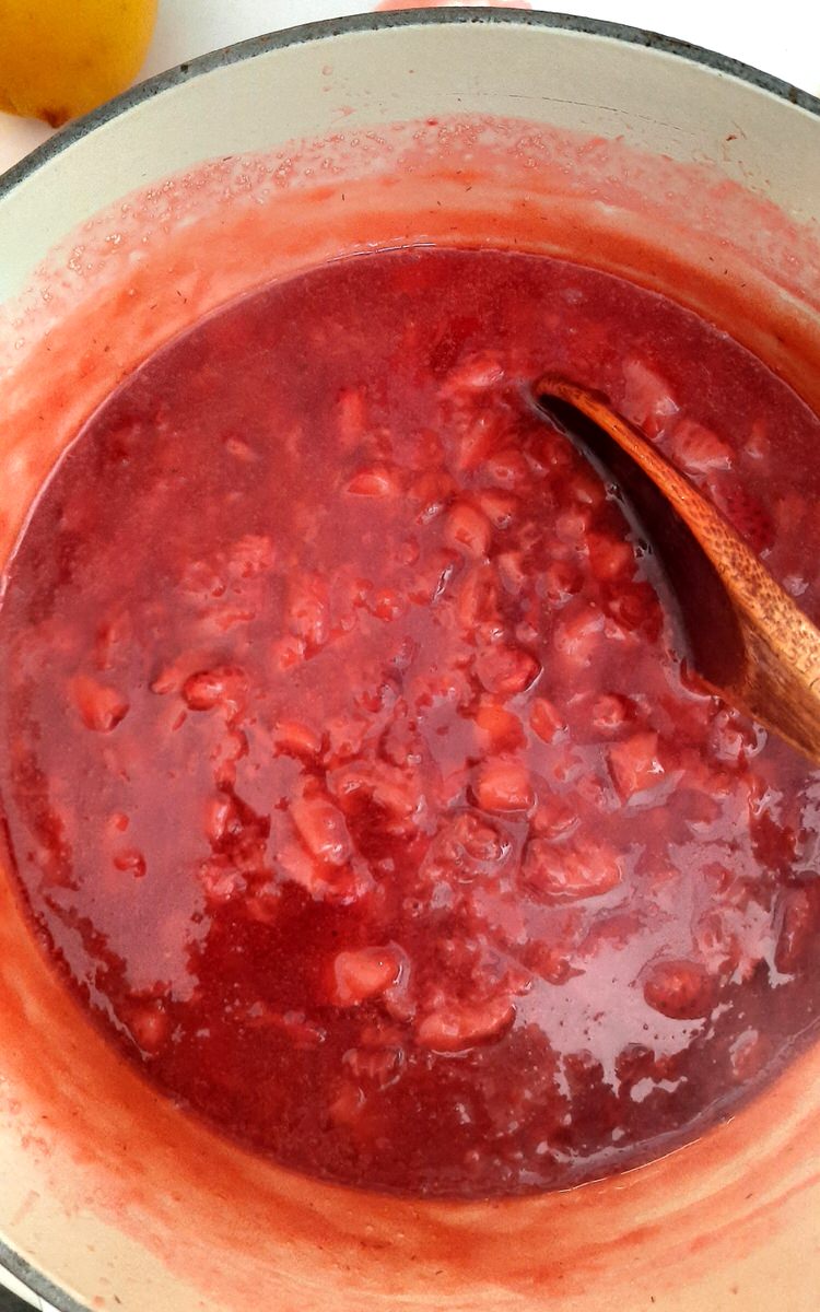 strawberries are crushed into a sauce in a sauce pan and are being stirred with a wooden spoon