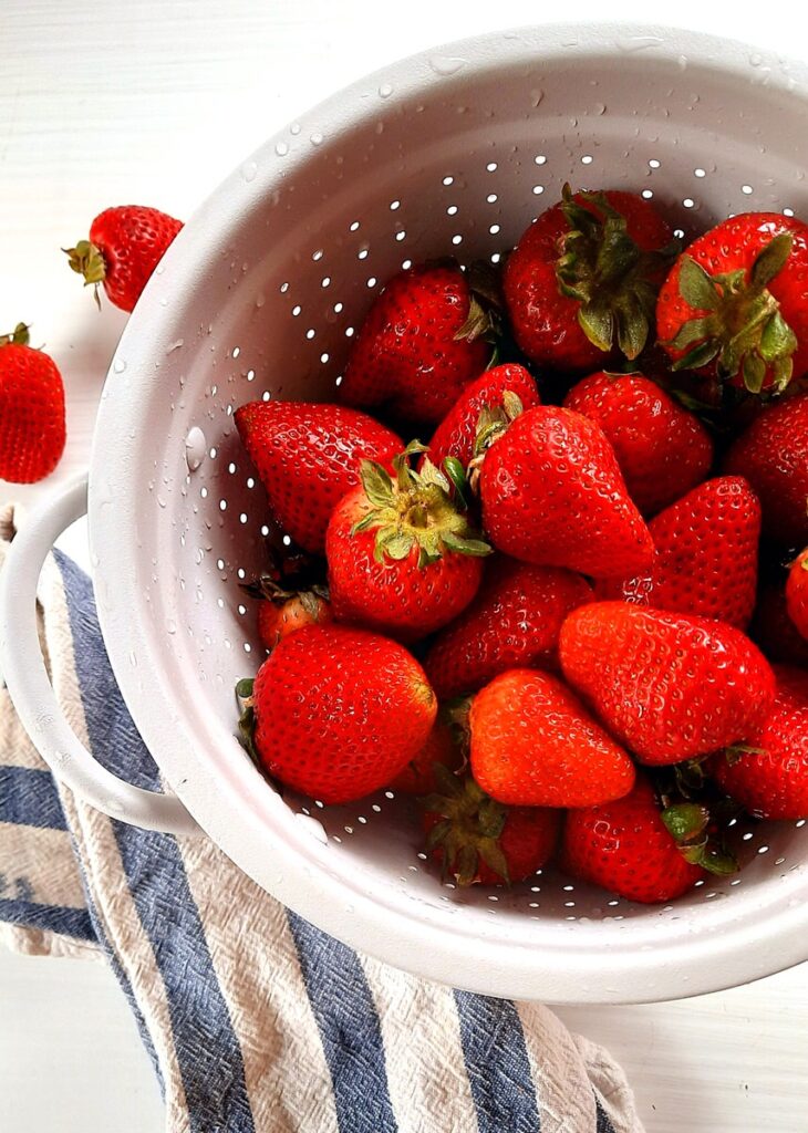 a white colander filled with fresh strawberries