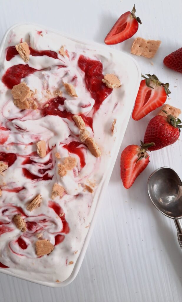 a white pan with ice cream and strawberry swirl and graham crackers on the top