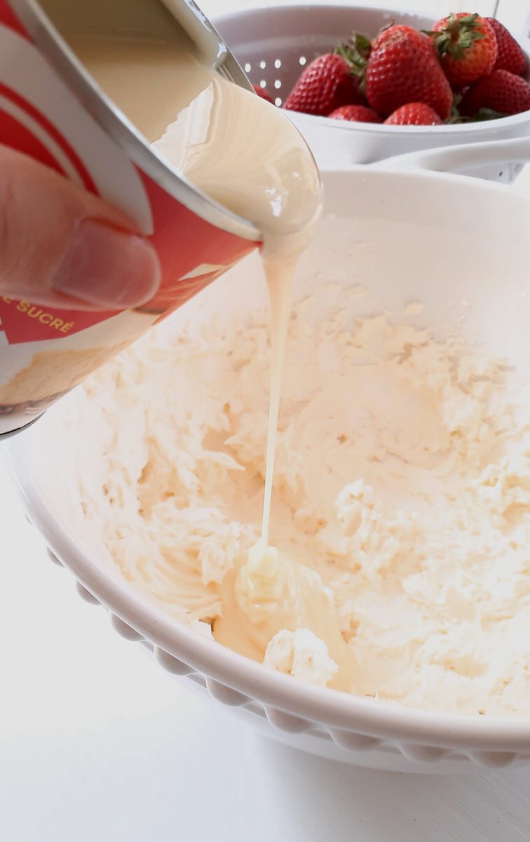 pouring sweetened condensed milk into a bowl of whipped cream cheese