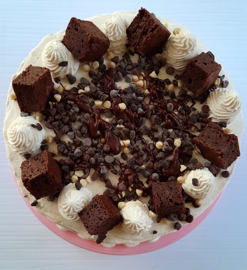 top shot of brownie ice cream cake covered in whipped cream, brownie pieces, and chocolate chips
