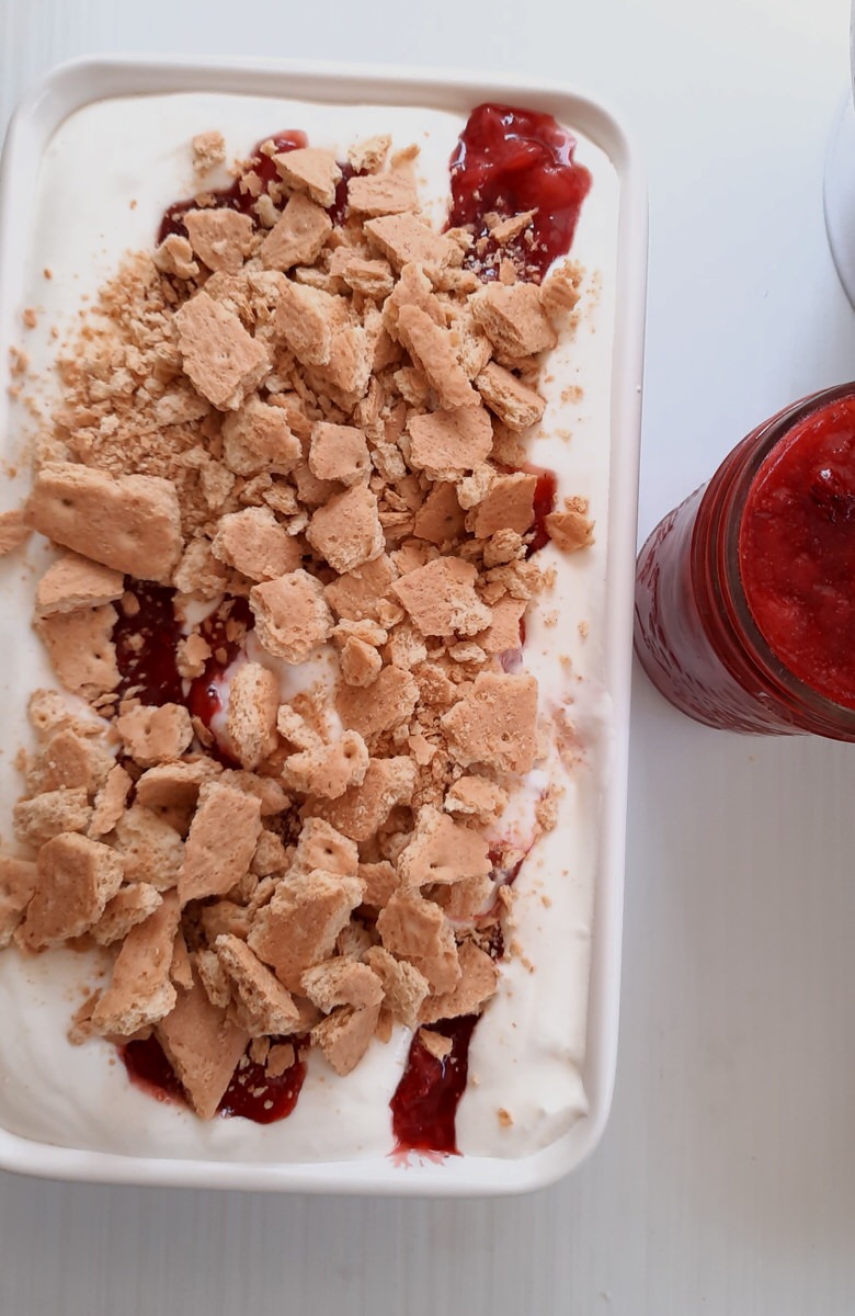 no churn ice cream in a loaf pan topped with a pile of strawberry sauce and graham cracker pieces