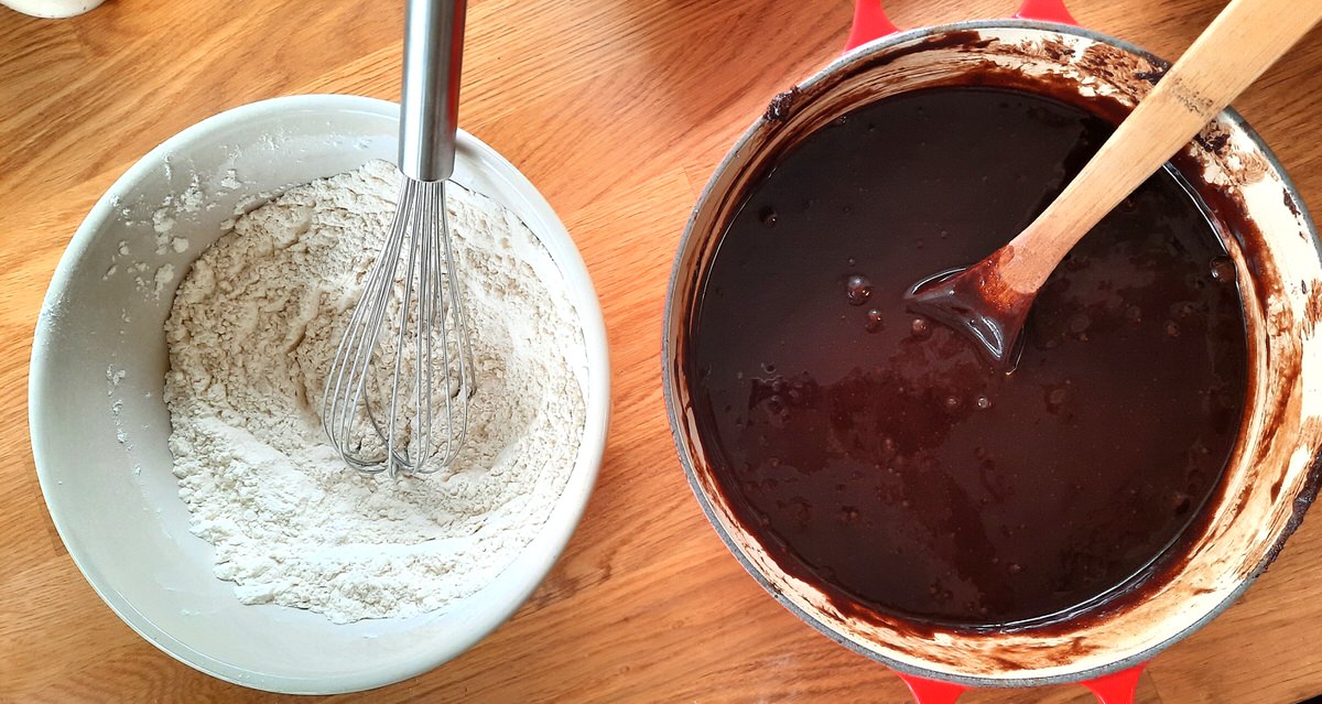 a bowl of dry ingredients sits on a counter beside a bowl of melted chocolate and wet brownie ingredients