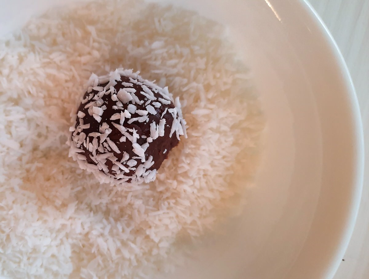 a ball of truffle is rolled in shredded coconut