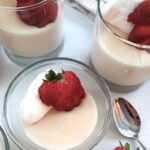 clear glass cups of homemade vanilla pudding topped with whipped cream and stawberries