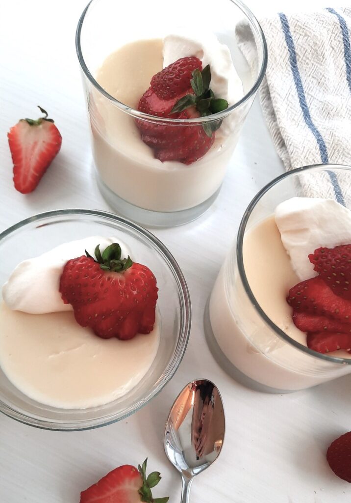 glasses of vanilla pudding garnished with strawberries and whipped cream