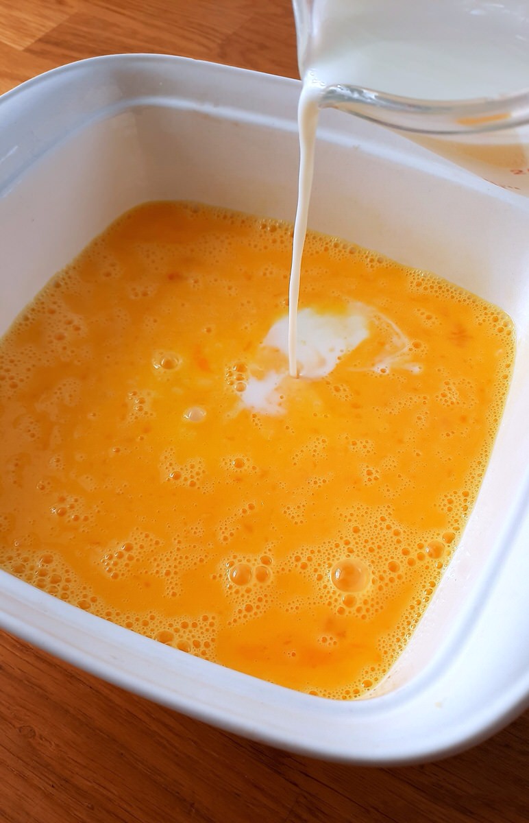 milk being poured into baking dish with whisked eggs