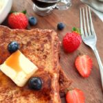 french toast piled on a wooden board surrounded by berries