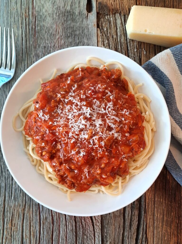 spaghetti and meat sauce in a white bowl on a rustic wood counter