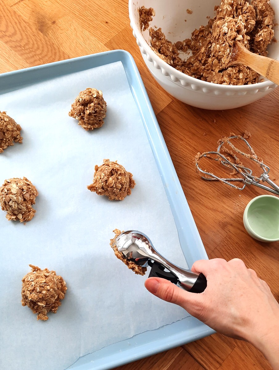 a hand scoops salted caramel oatmeal cookie dough onto a baking sheet