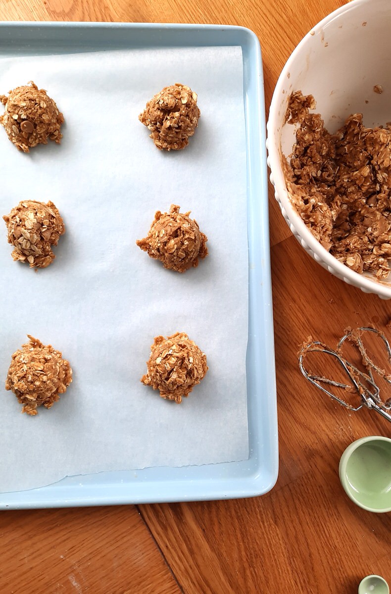 a tray of raw oatmeal cookies sits beside a bowl of oatmeal cookie dough