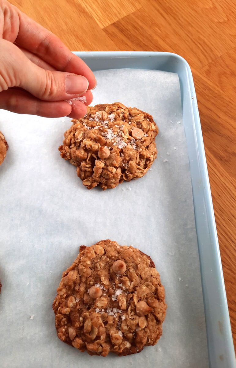 sprinkling flaked sea salt onto baked salted caramel oatmeal cookies