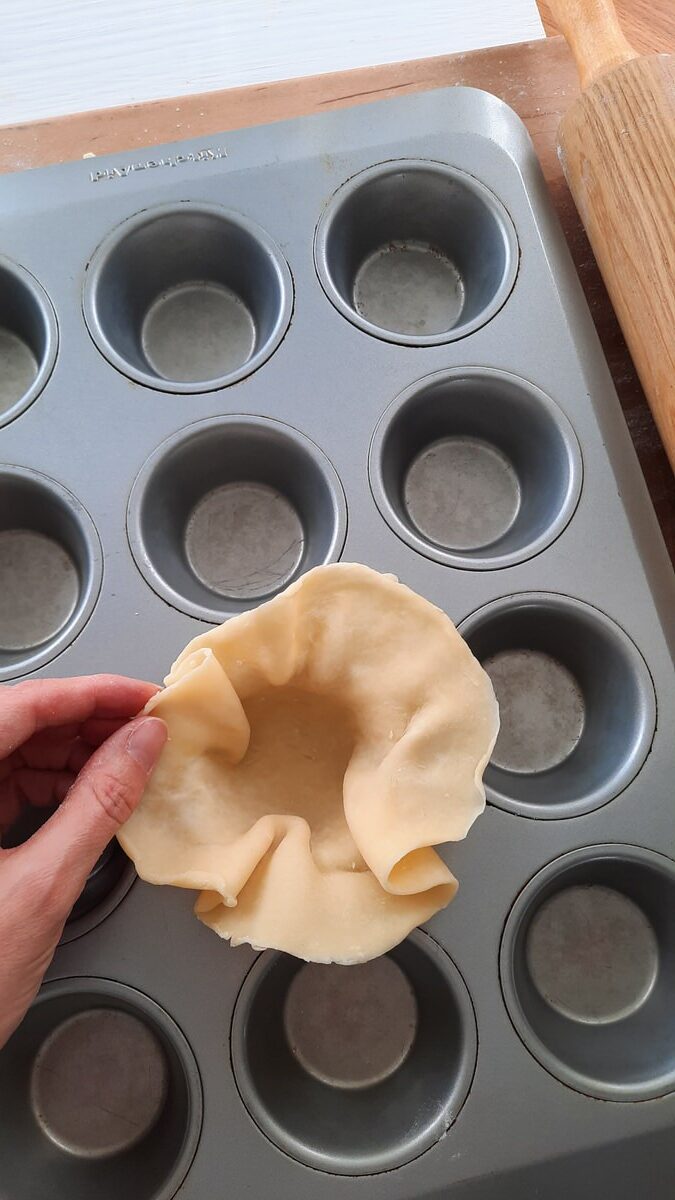 a hand carefully presses pie dough into a muffin tin