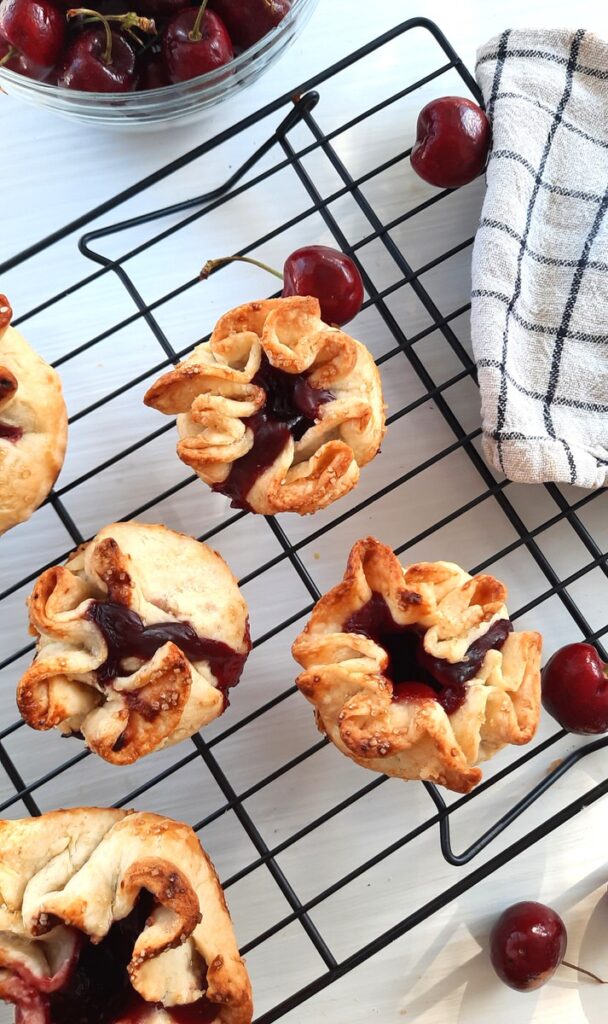 mini cherry pie rosettes on a cooling rack with cherries and a rolling pin