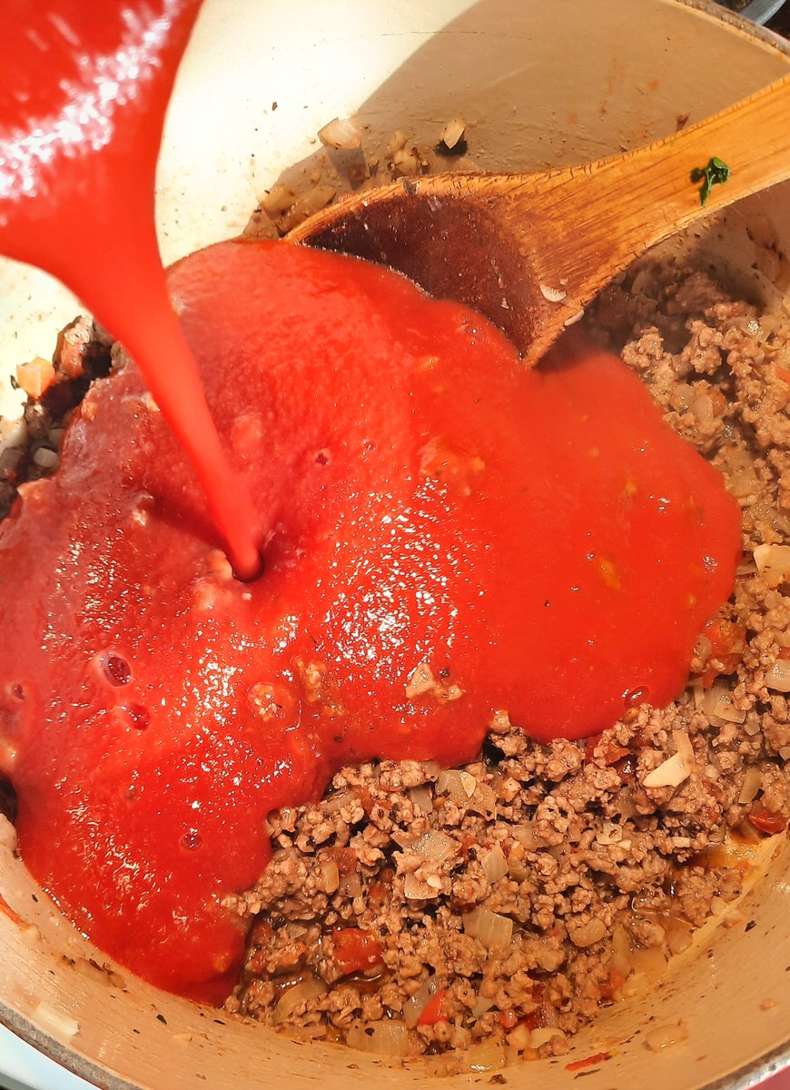 tomato sauce pouring into a pan of cooked ground beef