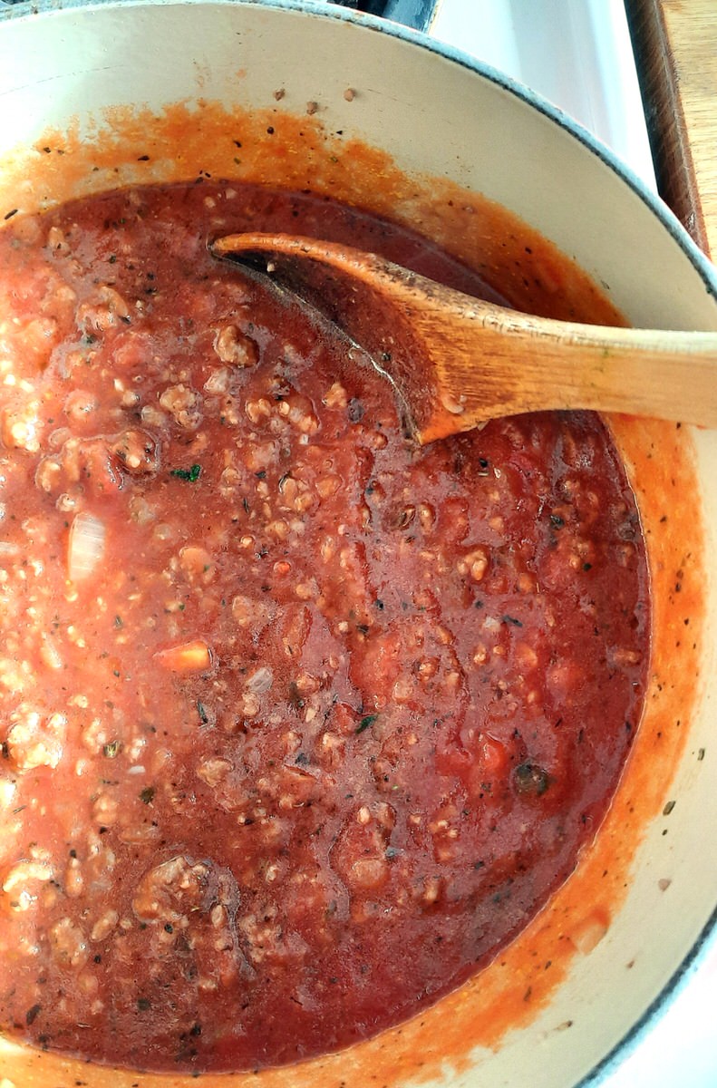 tomato meat sauce being stirred with a wooden spoon