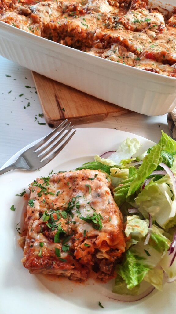 a large slice of homemade lasagna on a white plate with salad