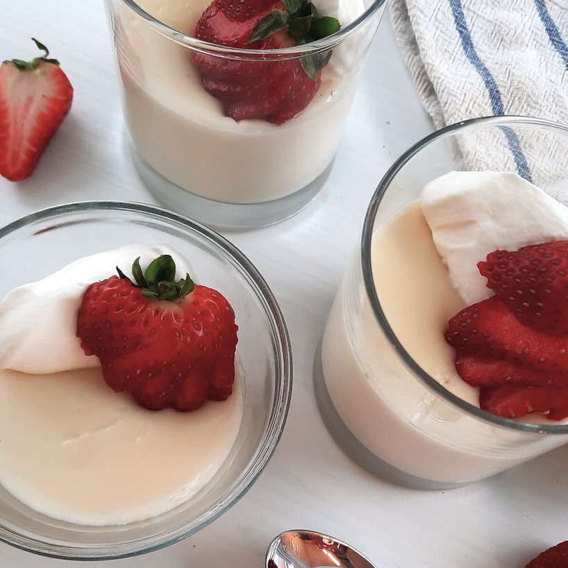 close shot of homemade vanilla pudding in glass cups garnished with cream and berries