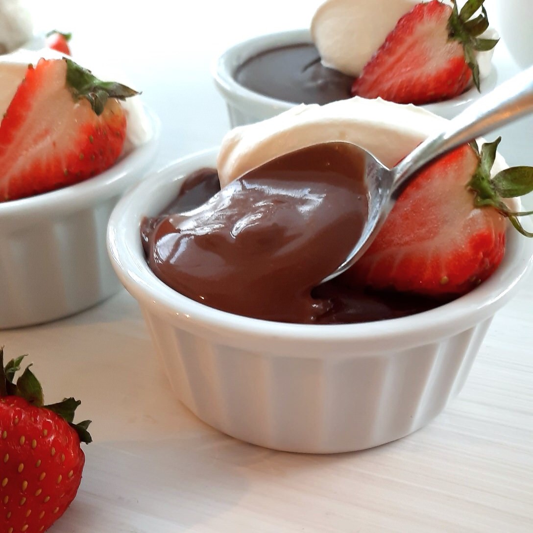 close shot of a small bowl or chocolate pudding and a spoon of creamy rich pudding on a spoon