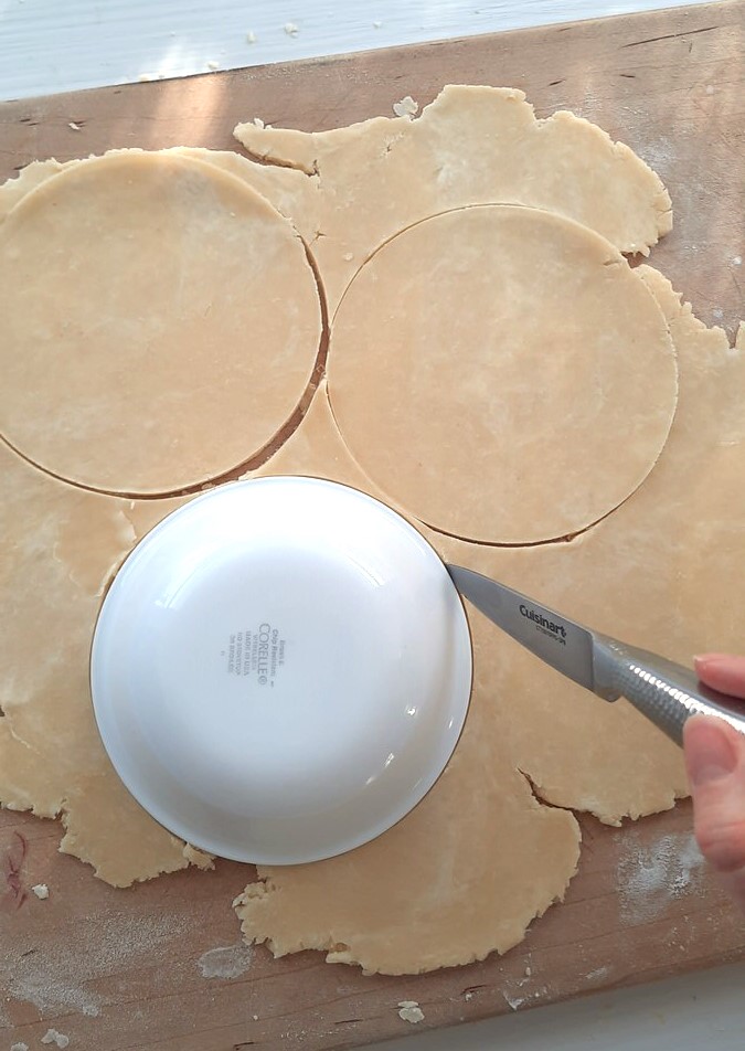 a hand cuts around an inverted bowl to make rounds of pie dough for hand pies