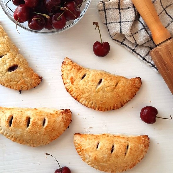 multiple hand pies on a counter with cherries scattered around