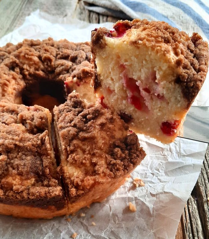 a slice of cranberry coffee cake being lifted away from the full cake with cranberries and crumble topping