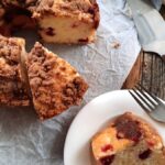 a slice of cranberry coffee cake on a white plate beside a whole coffee cake