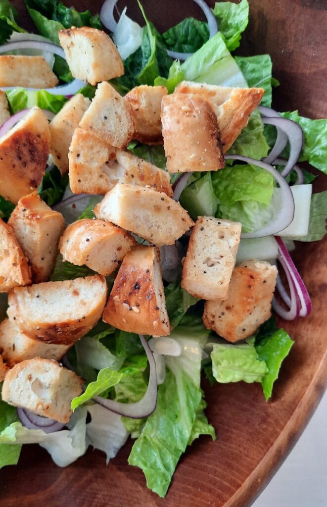 close up of bagel croutons on a salad in a wooden bowl