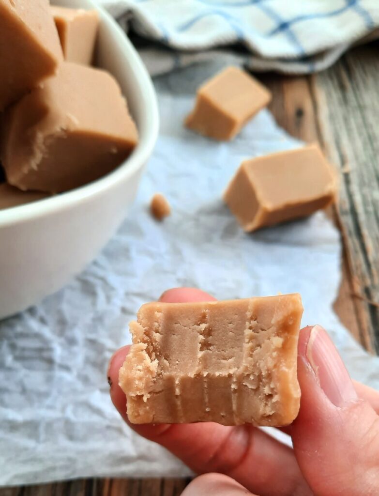 a hand holds up a piece of creamy maple fudge with a bite out of it