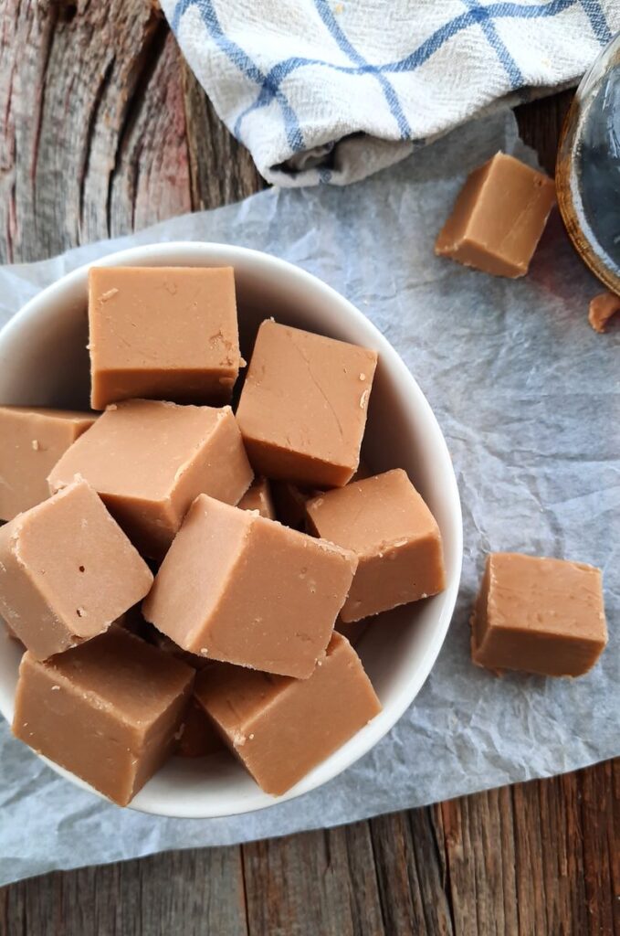 creamy maple fudge squares are piled into a white bowl and spilling over onto the counter