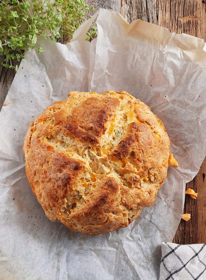 Cheddar Irish Soda bread sits on parchment paper on a wooden counter