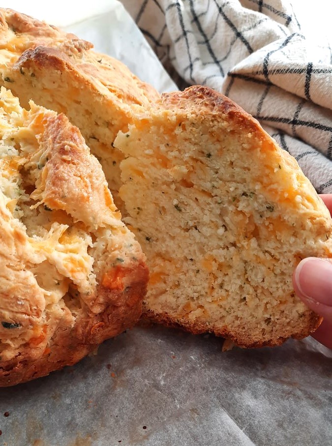 a hand removes a slice of cheddar soda bread from the loaf