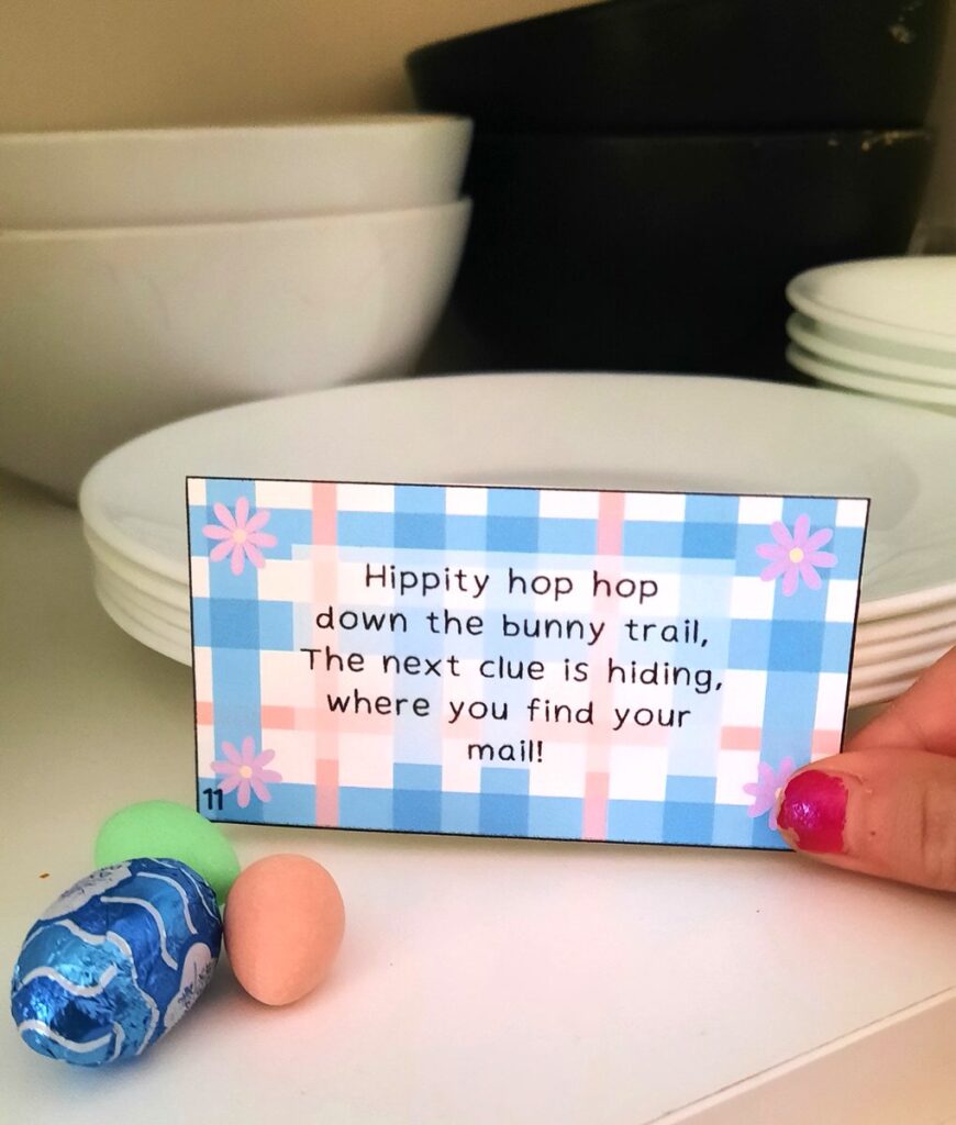a little girl's hand pulls and easter scavenger hunt clue out from its hiding spot among dishes in a cupboard