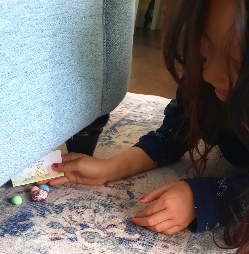 a little girl finds an easter scavenger hunt clue and some chocolate eggs under a sofa