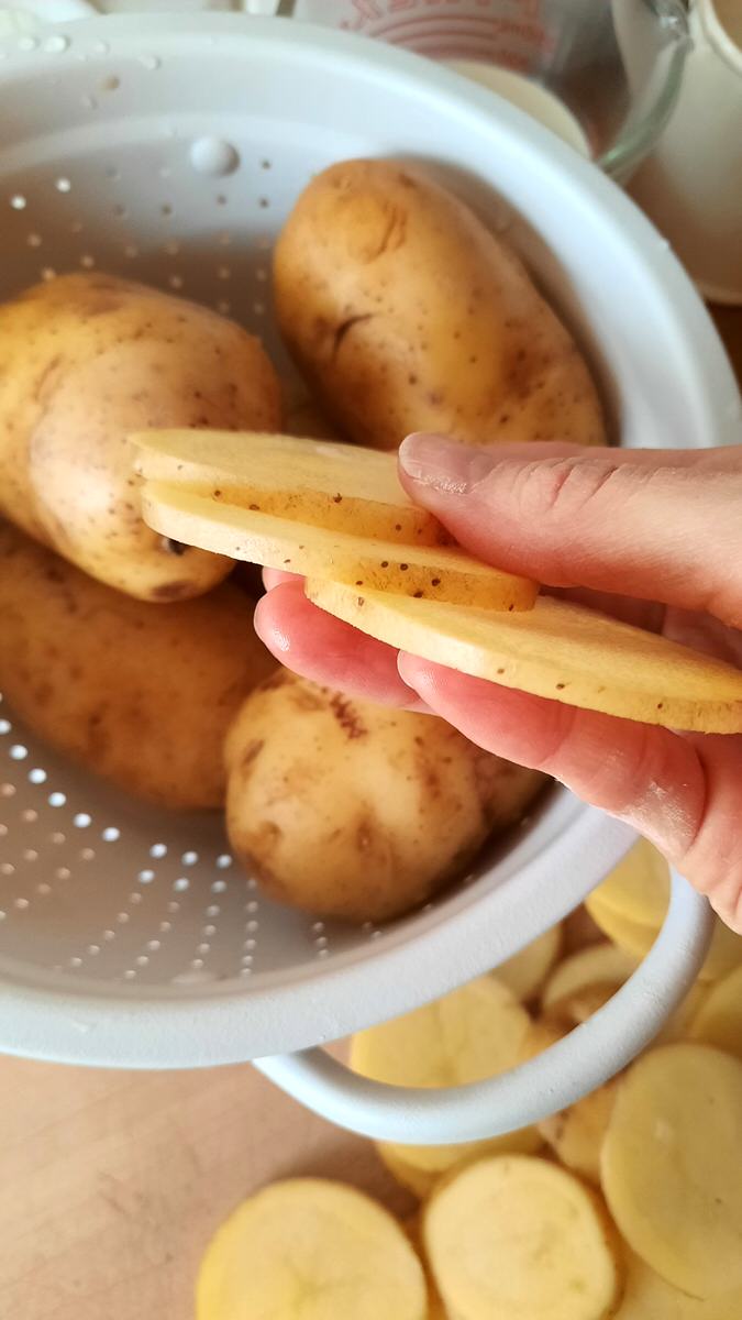 a hand holds three evenly sliced Yukon Gold potatoes