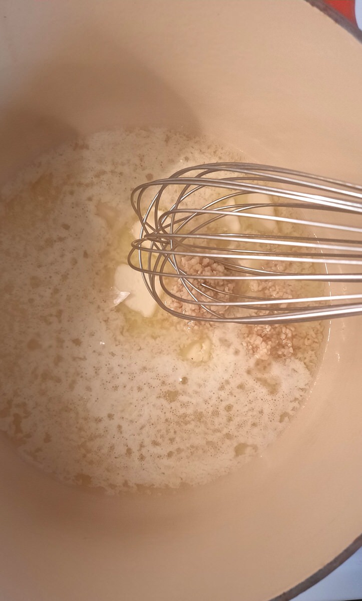 a whisk stirs together melted butter and garlic in a dutch oven