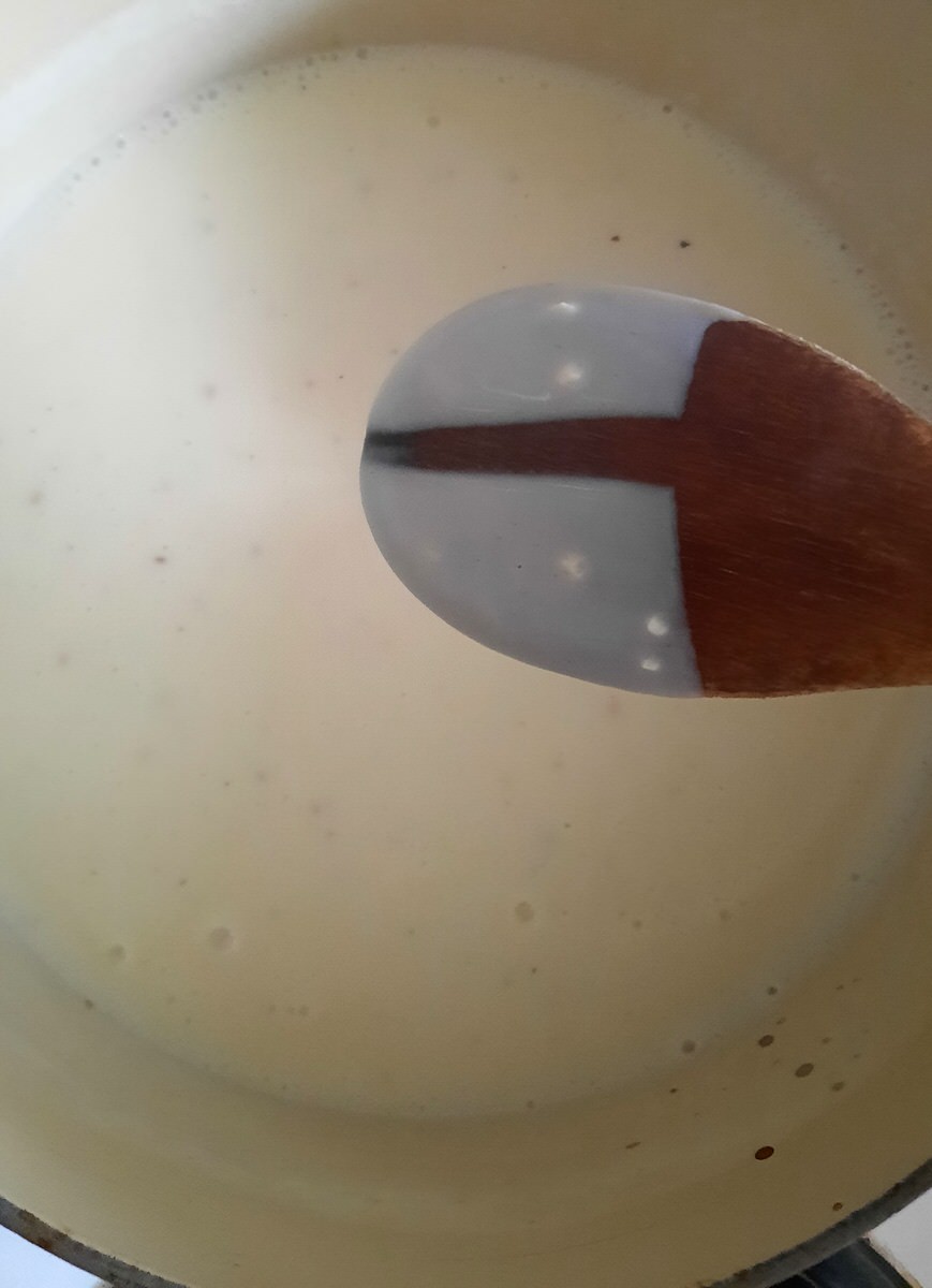 a wooden spoon coated in cream sauce with a finger line running through it shows the sauce is thickened perfectly