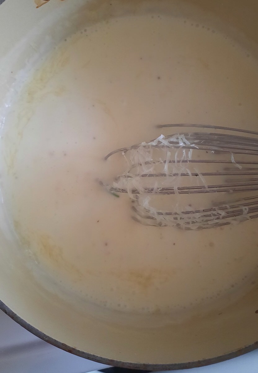 whisking grated asiago cheese into a pot of cream sauce