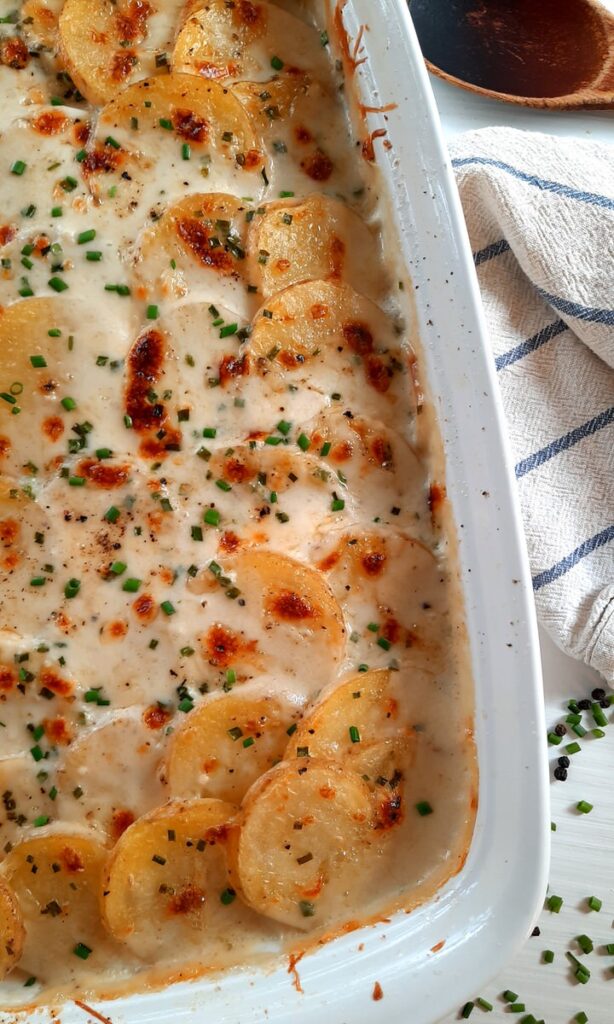a partial shot of a pan of scalloped potatoes with asiage, dijon, and chives
