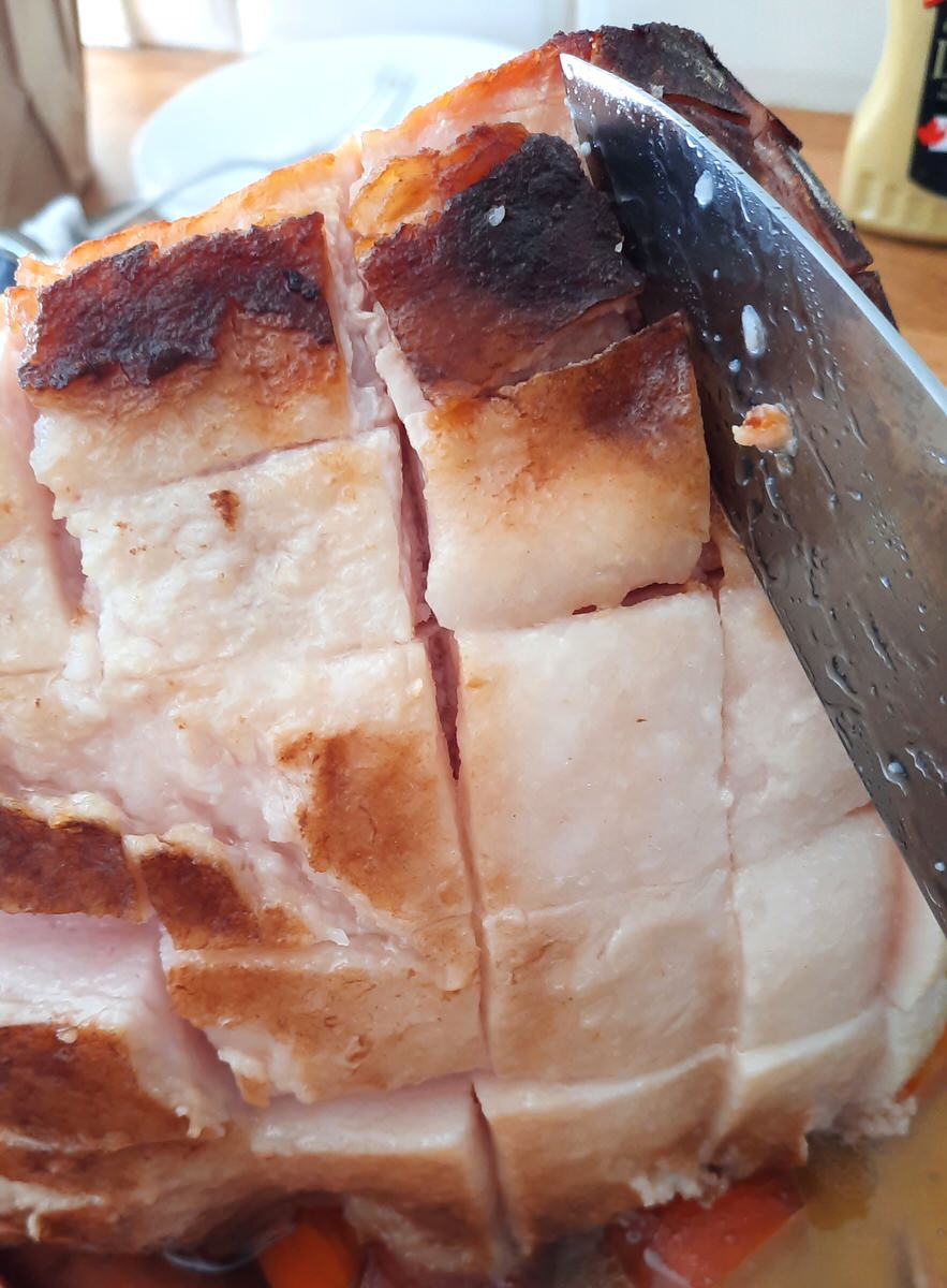a knife slices the skin of a cooked ham in a grid pattern
