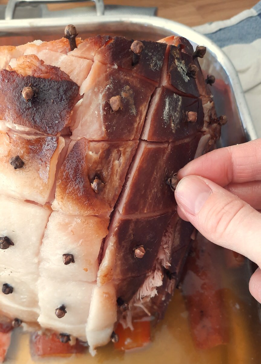 a hand places whole cloves all over the top of a cooked ham