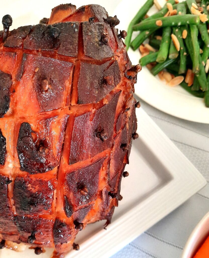 a shot of part of a baked ham with honey mustard glaze on a table beside some steamed green beans