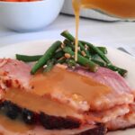 slices of baked ham sit on a plate while honey mustard sauce is drizzled on it